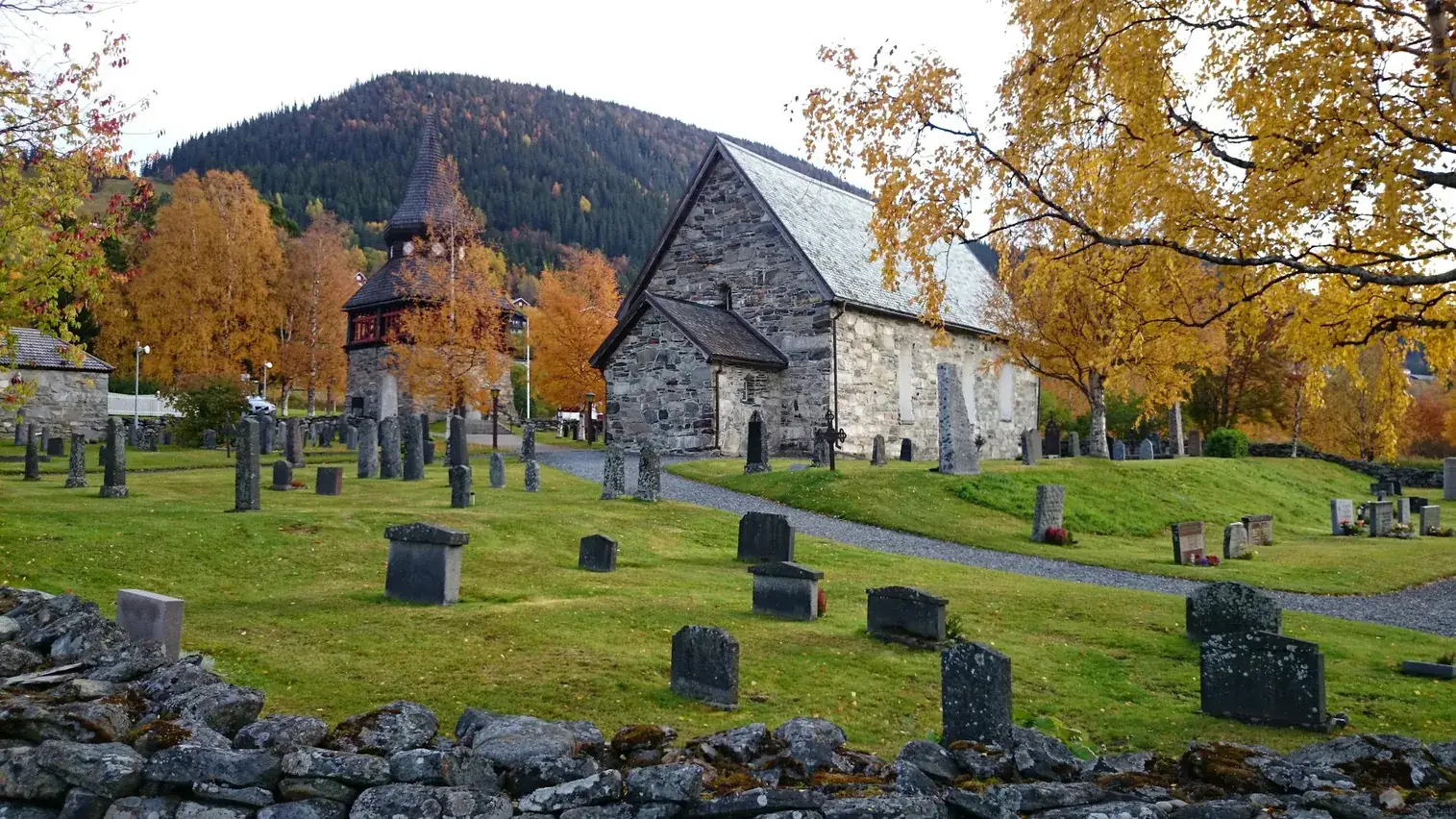 Åre gamla kyrka en höstdag med gula björkar och fjällsluttningen bakom.