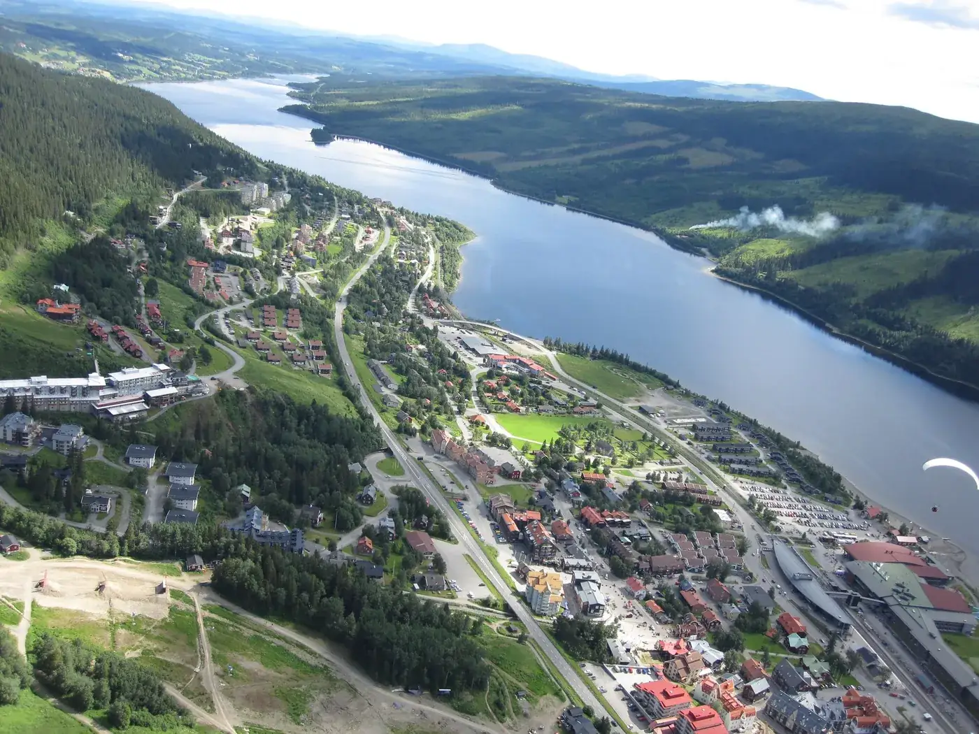 Flygbild över Åre by en sommardag, med bebyggelsen längs Åresjön och skidbackarna ovanför.