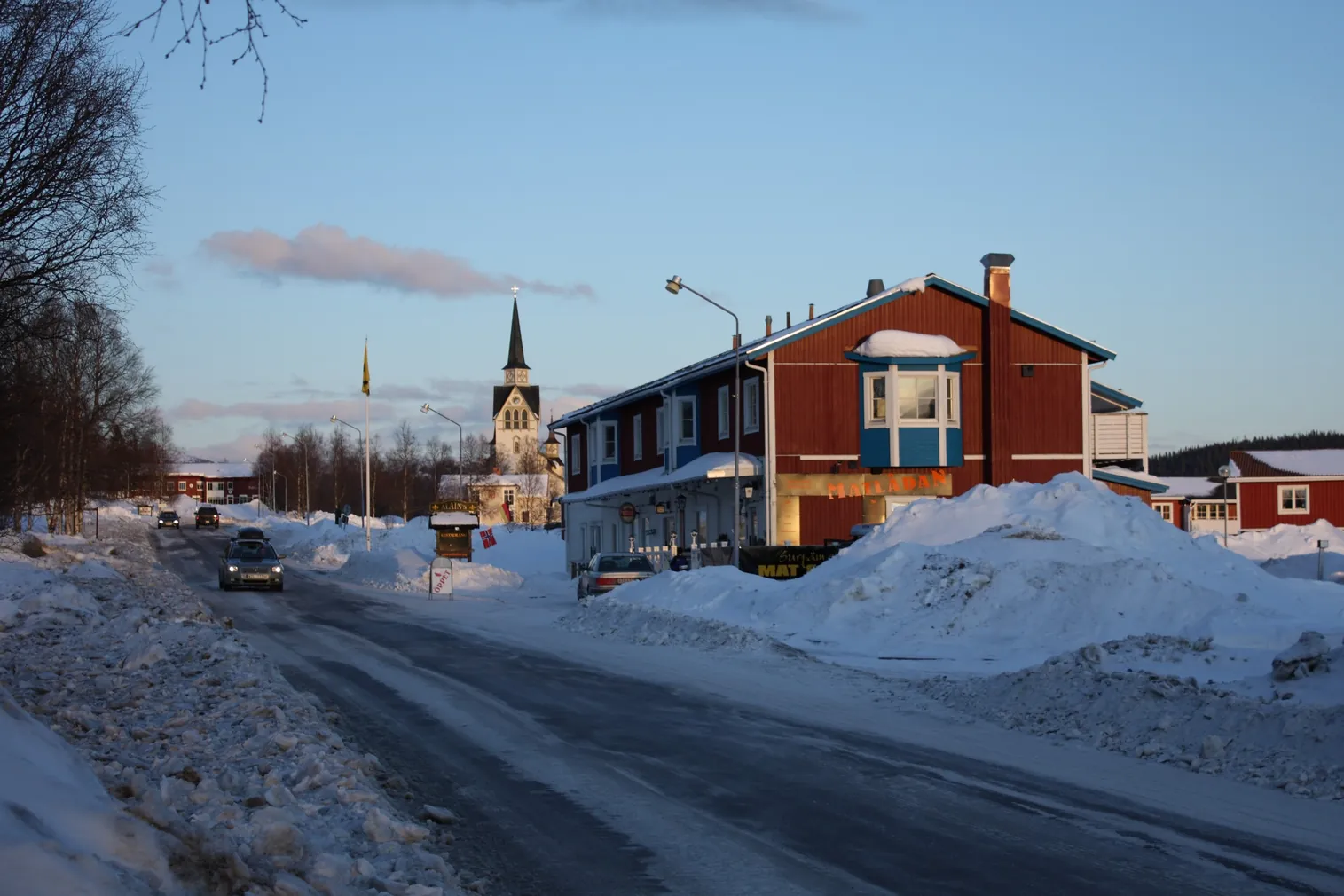 Bygatan i Duved en vinterkväll med snövallar, röda hus och Duveds kyrka.